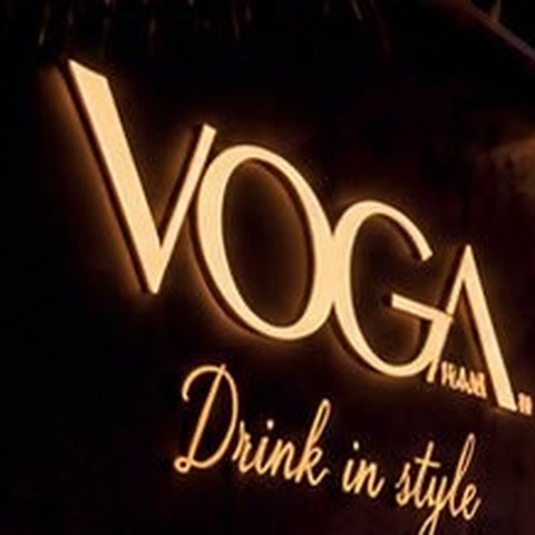 Insegna luminosa VOGA Drink in style dietro il bancone